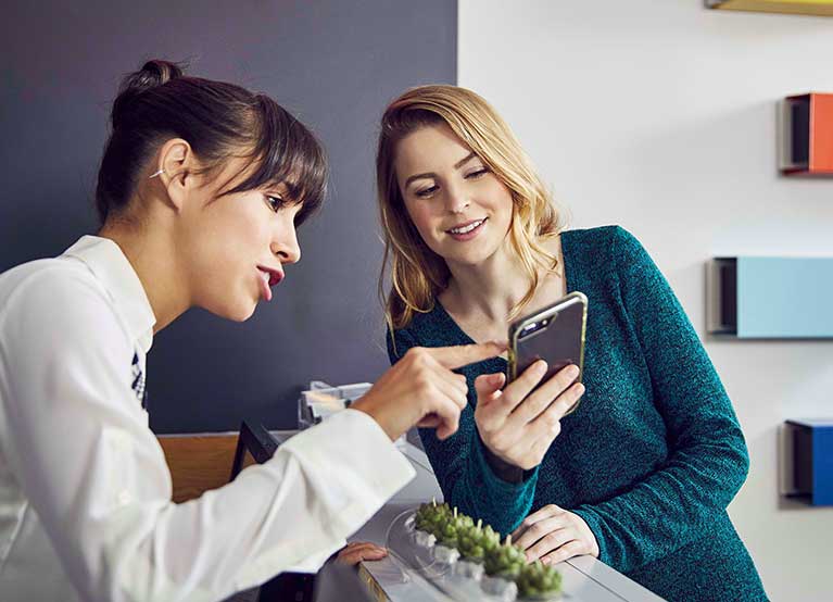 Two ladies looking at a phone in a dentist office. - 767x554.jpg