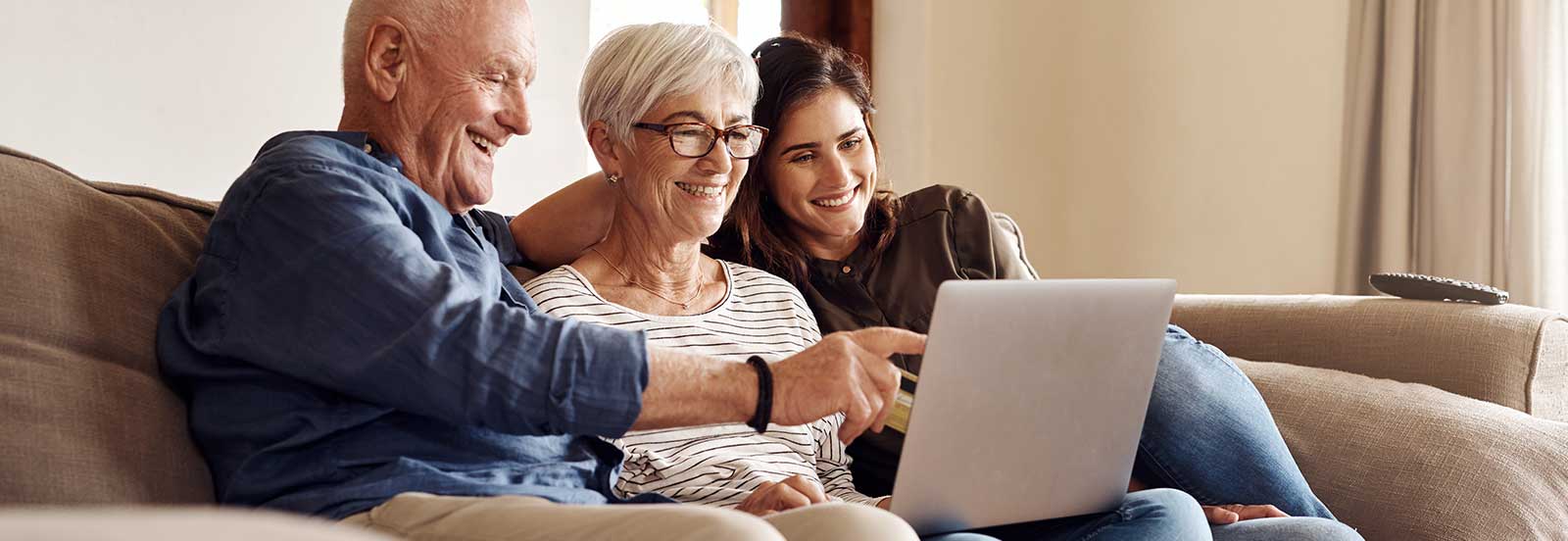 Older couple with a computer sitting next to a young lady on the couch. - 1600x552.jpg